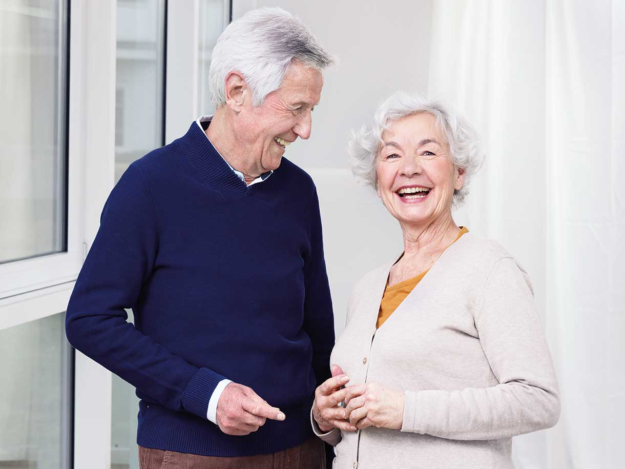 Пожилые мужчина и женщина стоят рядом и улыбаются